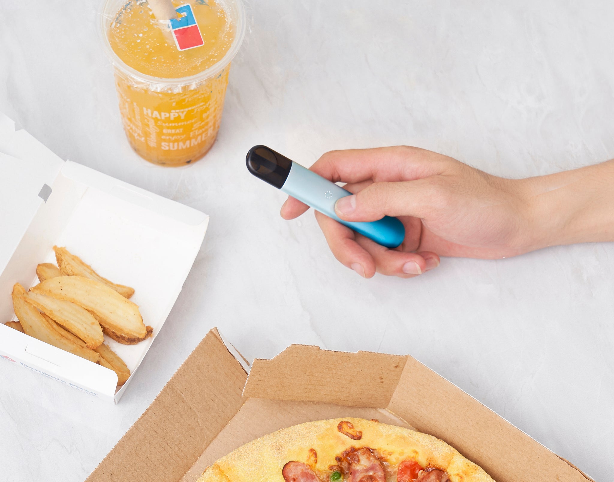 Seseorang memegang device RELX Infinity warna biru dengan makanan dan minuman di dekatnya.