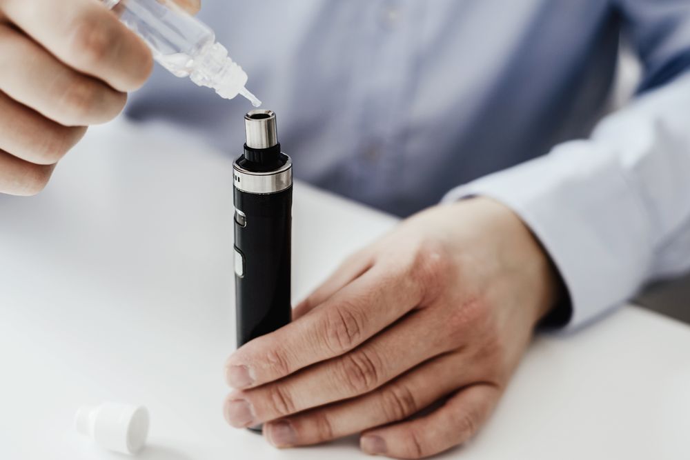 Seorang pria mengisi ulang vape pod dengan e-juice baru di atas meja