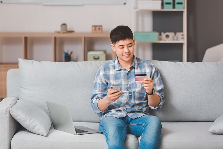 Seorang pria sedang memegang ponsel dan kartu kredit di sofa