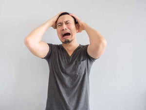 Seorang pria berbaju abu-abu sedang memegang kepalanya dengan ekspresi menangis