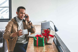 Seorang pria asyik menelpon dan menikmati kopi di kantor sambil menyiapkan bingkisan akhir tahun