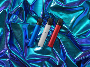 Tiga buah vape pod RELX Essential di atas latar holographic warna ungu dan tosca